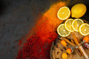top view of colorful spices with lemon slices kumquats and cinnamon sticks on black background